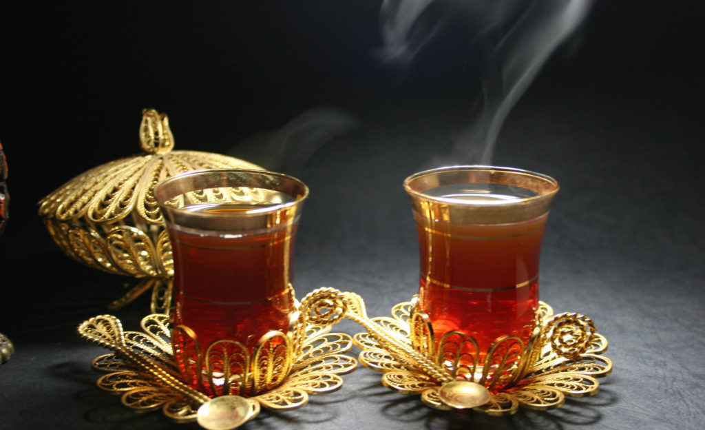 Two gold-edged glasses holding steaming black tea.