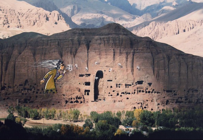 Graffiti of a woman in year with free-flowing hair, blowing dandelion seed heads, on the side of a mountain with doors and windows carved into it.