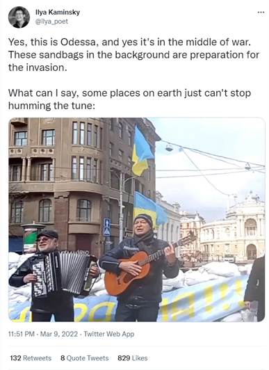Tweet from @Ilya_poet with the caption "Yes, this is Odessa, and yes it's in the middle of war. These sandbags in the background are preparation for the invasion. What can I say, some places on earth just can't stop humming the tune:" Attached photo is of two Ukrainian men playing an accordion and guitar in front of sandbags in a city block. with Ukrainian flags in the background
