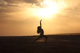 A silhouette of a dancer in a lunge with her arms up, against a sunset
