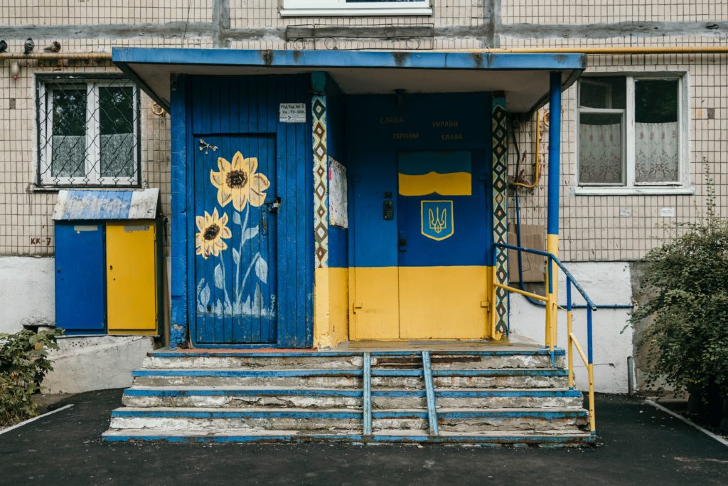 A front porch stoop painted in the yellow and blue of the Ukrainian flag. Yellow sunflowers, the Ukrainian national flag, painted against a blue door.